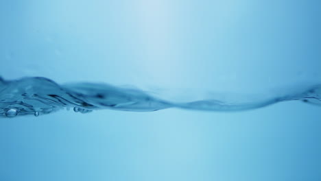 Splattering-water-creating-tiny-droplets-and-ripples-in-a-container-filled-with-water-against-a-blue-background