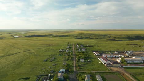 Filas-De-Casas-Y-Una-Estructura-Privada-Situada-En-Campos-Verdes-Cerca-De-Un-Camino-De-Tierra-En-Kazajstán,-Asia-Central---Drones-Volando-Hacia-Adelante