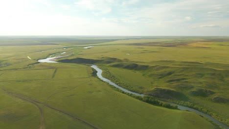 Una-Vista-De-Un-Río-Que-Fluye-En-Medio-De-Extensos-Campos-Verdes-En-La-Región-Rural-De-Kazajstán,-Asia-Central---Disparo-Aéreo-De-Drones