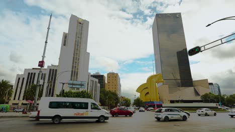 Vehicles-circulating-on-crossroads-Paseo-de-la-Reforma-and-Bucareli-Avenue-with-buildings-and-sculpture-in-background,-Mexico-City