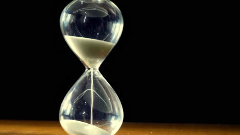 Closeup-of-time-sand-timer-clock-with-sand-flowing-from-through-hourglass-on-black-background