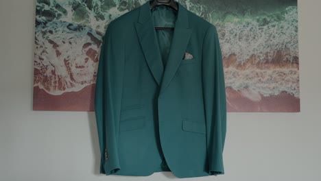 Teal-suit-jacket-hanging-on-a-hanger-with-a-beach-themed-background,-highlighting-stylish-wedding-attire