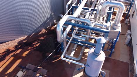 Drone-shot-moving-up-and-over-metal-pipes-and-infrastructure-at-an-industrial-facility