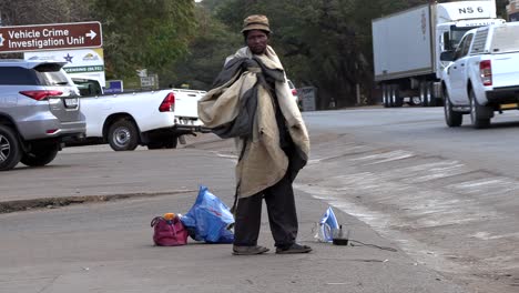 A-local-African-man-wraps-an-old,-worn-blanket-around-himself-on-a-sidewalk