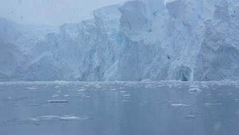 Antarctica-Coast-on-Snowy-Day,-Massive-Glacier-and-Pieces-of-Ice-in-Cold-Ocean-Water