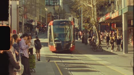 Super-8-vintage-film-of-tram-approaching-platform-in-middle-of-Sydney-city-CBD-Pitt-George-street-roads-with-people-waiting-Australia-transport-travel-light-leaks