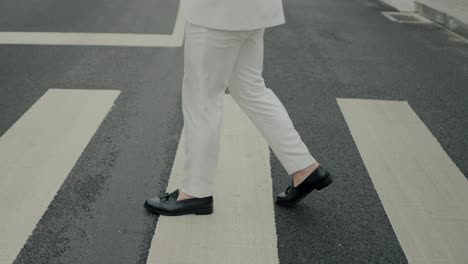 Groom-in-white-trousers-and-black-shoes-crossing-a-street,-highlighting-modern-wedding-style