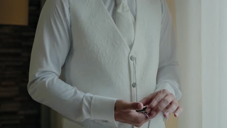 Groom-in-a-white-vest-holding-a-pocket-watch,-highlighting-elegant-wedding-preparation