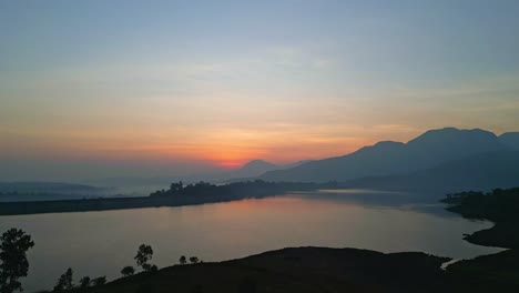 Ein-Ruhiger-Und-Wunderschöner-Sonnenuntergang-Am-Arthur-Lake-Und-Den-Bergen-Am-Horizont-Im-Distrikt-Bhandardara-Ahmednagar-In-Maharashtra,-Indien,-4K-Drohne