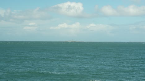 Scenic-view-of-Tiwai-Point-with-a-distant-lighthouse-across-the-calm-ocean-waters-under-a-partly-cloudy-sky