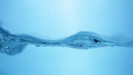 Close-up-shot-of-crystal-clear-blue-waters-bursting-into-waves,-creating-splatters-and-bubbles-in-a-big-water-tank