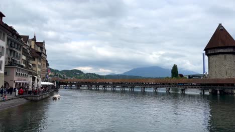 Panning-shot-of-Chapel-Bridge-in-Lucerne-old-town-with-walking-tourist-along-promenade