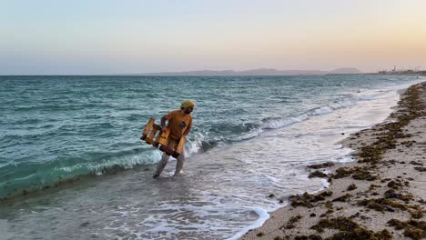 Junger-Mann-Zieht-Holzpaletten-Aus-Dem-Meer-Am-Sandstrand-Der-VAE-In-Der-Dämmerung,-Heimat-Der-Karettschildkröte.-Bemühungen-Unterstreichen-Die-Bedeutung-Des-Schutzes-Des-Meereslebens-Und-Der-Erhaltung-Sauberer-Strände-In-Iran-Und-Katar.-Natur