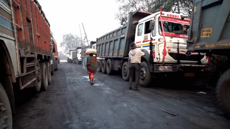 Frau-Trägt-Kohle,-Minenfahrzeuge-Für-Den-Kohletransport-Warten-Auf-Die-Beladung-Im-Kohlefeld-Jharia,-Dhanbad,-Jharkhand