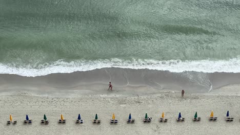 People-walk-along-the-shore-of-Myrtle-Beach-in-slow-motion-with-closed-umbrellas-and-waves-crashing