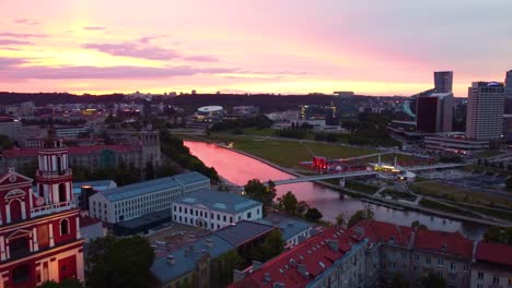 Aerial-pink-sunset-view-of-Vilnius,-Lithuania-with-reflections-on-river