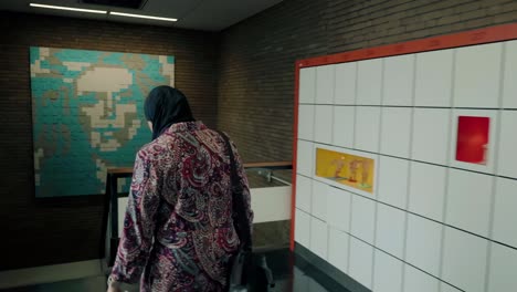 Rear-view-of-a-Muslim-woman-with-a-headscarf-walking-through-a-school-corridor-with-art-on-the-wall