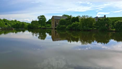 Drone-flying-over-water-surface-of-Mayenne-River-with-Saint-Baudelle-lock-or-weir-in-background,-France