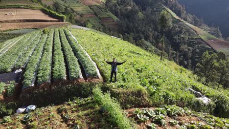 Drone-reverse-shot,-traveler-waving-at-the-drone-showing-a-view-of-the-slopes-of-Mount-Sumbing