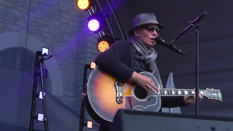 Footage-features-a-man-waring-a-hat-singing-and-playing-an-acoustic-guitar-on-a-stage-in-slow-motion-shot-in-4K-in-Tallinn,-Estonia,-Europe