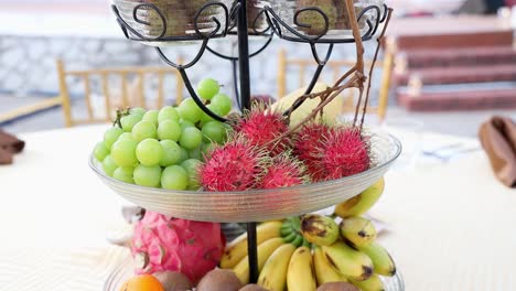 Close-up-of-a-tiered-tray-with-rambutan,-grapes,-bananas,-red-dragonfruit,-oranges,-kiwi-and-lychee-at-a-wedding-reception