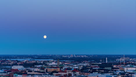 Time-lapse-of-the-full-moon-setting-above-the-Kallio-cityscape,-dawn-in-Helsinki