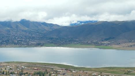 Aerial-drone-view-of-a-calm-lake-with-epic-cloudy-mountains-in-the-background,-slowmotion-and-copy-space