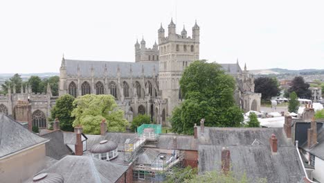 Órbita-Aérea-Alrededor-De-La-Catedral-De-Exeter,-Mostrando-La-Histórica-Estructura-Gótica-Con-Chimeneas-De-La-Ciudad-En-Primer-Plano.