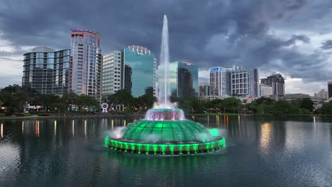 Beleuchteter-Brunnen-Des-Lake-Eola-Mit-Sprühendem-Wasser-Und-Moderner-Skyline-Im-Hintergrund