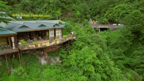 Distancing-aerial-view-of-a-couple-standing-on-traditional-houses-in-Sa-Pa,-nestled-in-Vietnam's-Hoàng-Liên-Son-Mountains