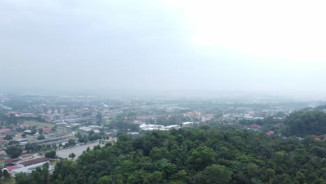 Lush-greenery-passes-under-the-drone-revealing-small-town-on-a-misty-midday-environment-in-Malaysia