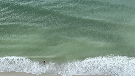 Man-Wades-at-the-edge-of-the-green-water-shore-at-Myrtle-Beach,-South-Carolina-in-slow-motion