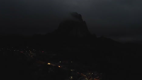 Bernal-city-in-Mexico,-aerial-at-night,-mountain-highlights,-lightly-lit