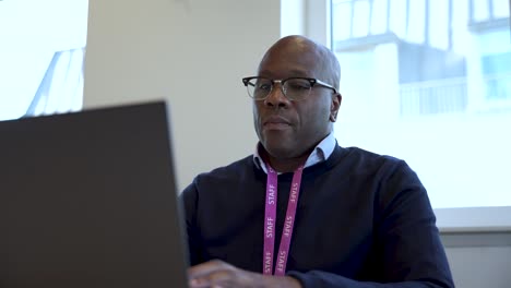 Bald-professional-man-wearing-glasses-and-eyewear-typing-on-a-laptop-in-an-office-environment-with-a-focused-expression