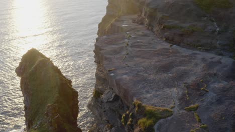 Aerial-shot-gliding-over-the-iconic-Flat-Edge-Surface-of-Cliffs-of-Moher,-revealing-its-depths-and-details-in-stunning-sunset-light