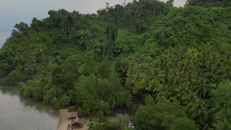 Drone-flying-over-a-remote-tropical-jungle-island-with-a-flat-and-calm-ocean-in-the-background