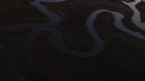 Meandering-river-snakes-through-open-wetland-swamps-at-sunset,-dark-moody-aerial-overview-Chincoteague-Island-Virginia,-slow-motion