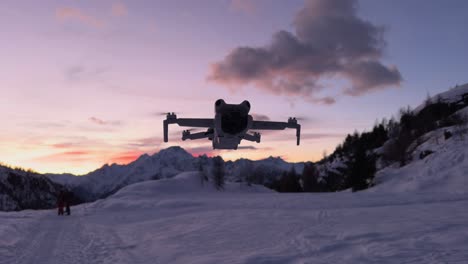 Close-up-of-lightweight-DJI-mini-series-drone-suspended-in-static-flight-with-sky-at-sunset-and-clouds-and-mountain-with-snow-in-background