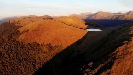 Vista-Aérea-De-Un-Tarn-De-Montaña-En-Una-Línea-De-Cresta-Alta-Bajo-El-Sol-De-La-Tarde