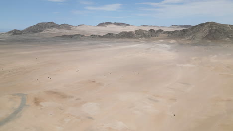 Aerial-of-a-wide-open-desolate-arid-desert-mountain-wilderness-with-yellow-sands,-grey-mountains-and-blue-sky-in-Namibia