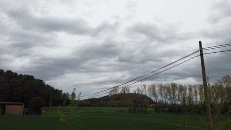 Zeitraffer-Eines-Feldes-Mit-Strommasten-Und-Bäumen,-Sehr-Bewölkter-Tag,-Kurz-Vor-Regen