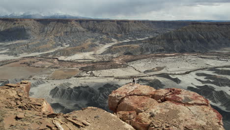 Drone-Shot-of-Woman-Standing-on-The-Edge-of-Cliff-Above-Abyss-and-Desert-Landscape