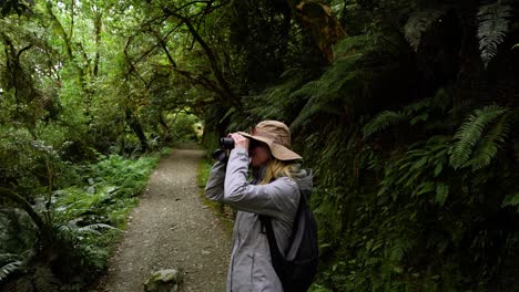 Girl-in-hat-with-camera-taking-pictures-in-peaceful-forest,-New-Zealand