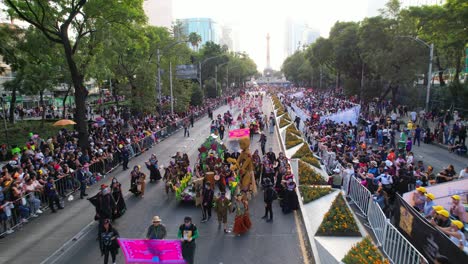 Mass-gathering-of-people-to-celebrate-Day-of-the-Dead-Parade-in-Mexico-City-streets,-Angel-of-Independence-monument-in-background