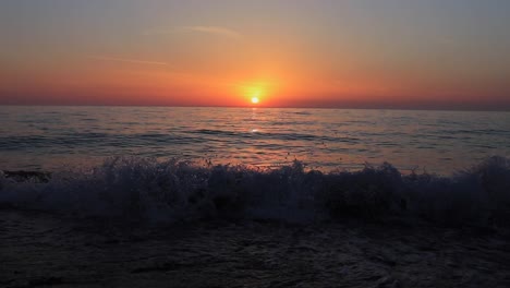 Sea-waves-splash-onto-the-shore-with-the-sun-setting-in-the-backdrop,-casting-evening-hues,-representing-the-concept-of-tranquility-and-natural-beauty