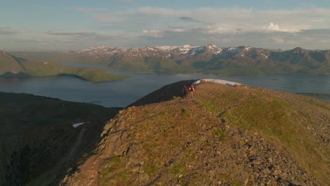 Hikers-on-husfjellet-mountain-in-senja,-norway-at-sunset-with-stunning-landscape,-aerial-view