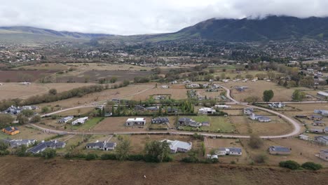 Dolly-drone-flight-of-building-area,-city-of-Tafi-del-Valle-with-the-cloudy-mountain-in-background,-aerial-in-slow-motion