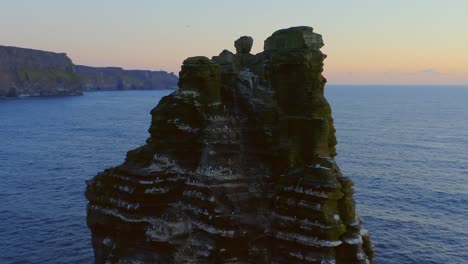 Stunning-aerial-orbit-around-bird-covered-sea-stack-at-Cliffs-of-Moher-during-vibrant-sunset