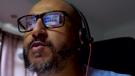 Close-up-of-a-South-Asian-trader-working-from-home,-wearing-glasses-and-a-headset-with-screen-reflections