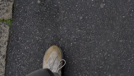 Close-up-of-dirty-sneakers-walking-over-asphalt,-showing-worn-footwear-and-rough-pavement-texture